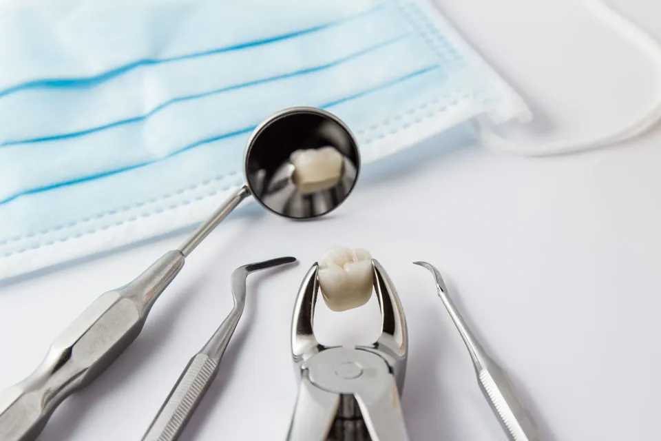Dental forceps holding a model tooth beside a dental mirror, probes and a face mask
