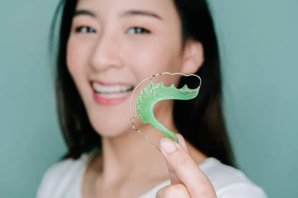 A smiling woman holding up a green removable retainer with a wire