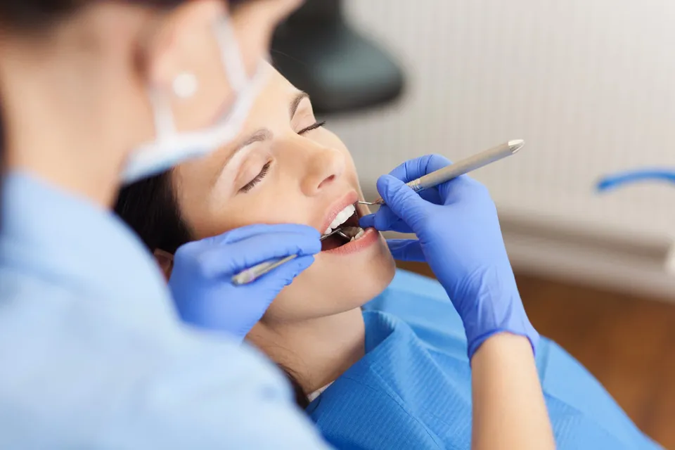 A dentist in blue gloves examining a woman's teeth with dental instruments